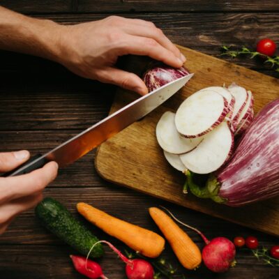 Person Slicing White Onion on Brown Wooden Chopping Board